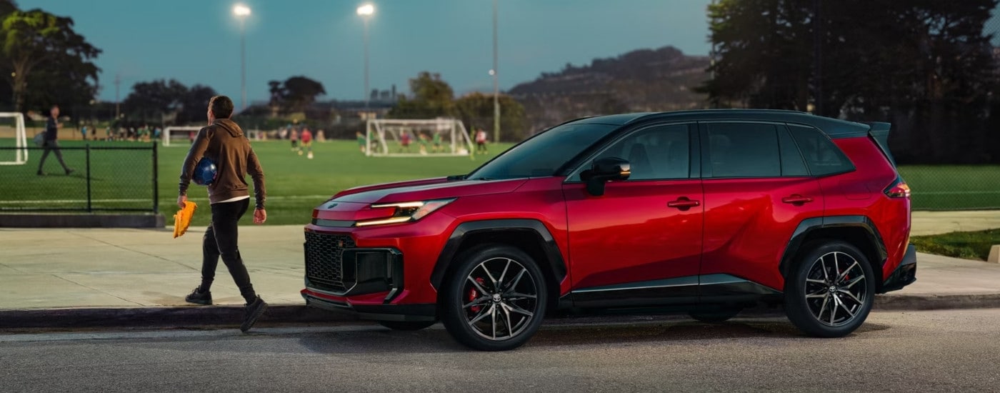 A red 2026 Toyota RAV4 PHEV GR Sport parked near a soccer field.
