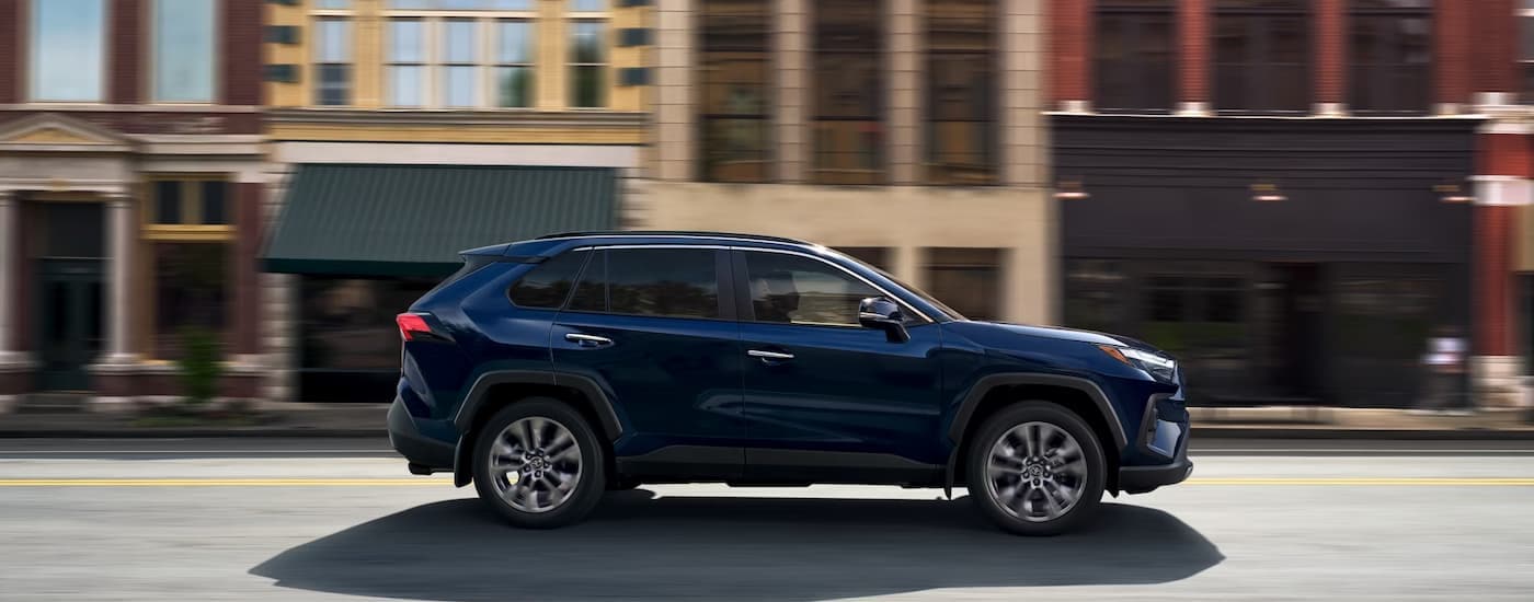 Side of a blue 2025 Toyota RAV4 Hybrid for sale near Nashville driving on a city street
