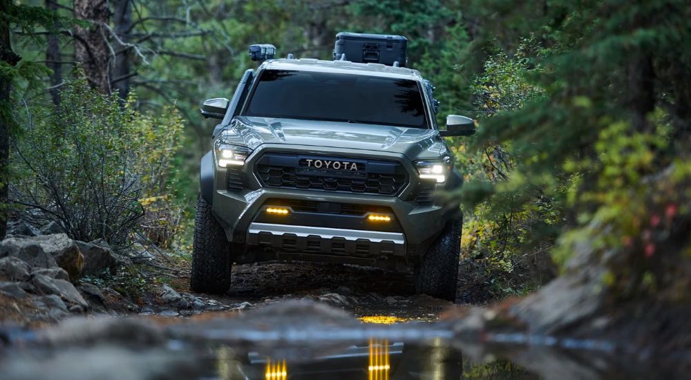 A green 2024 Toyota Tacoma Trailhunter is shown off-roading after visiting a Toyota dealer.