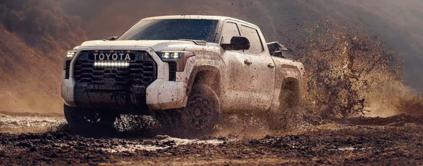 White 2026 Toyota Tundra TRD driving off-road over a mud puddle.