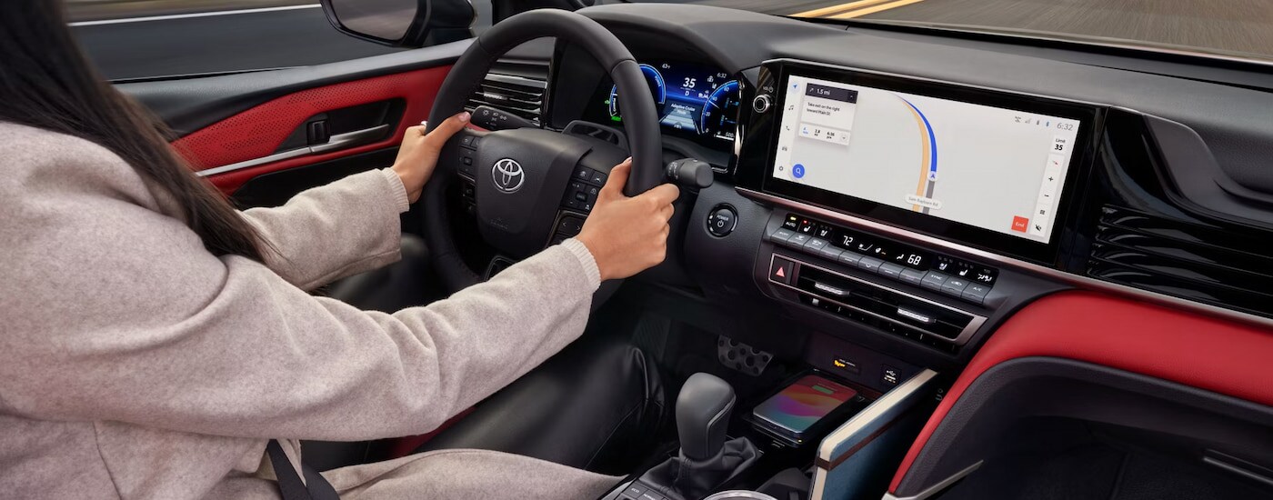 A woman driving in the red and black cabin of a 2025 Toyota Camry for sale.