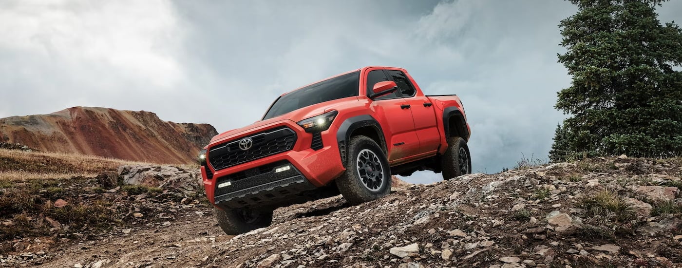 An orange 2024 Toyota Tacoma TRD Off-Road driving down a rocky hillside.