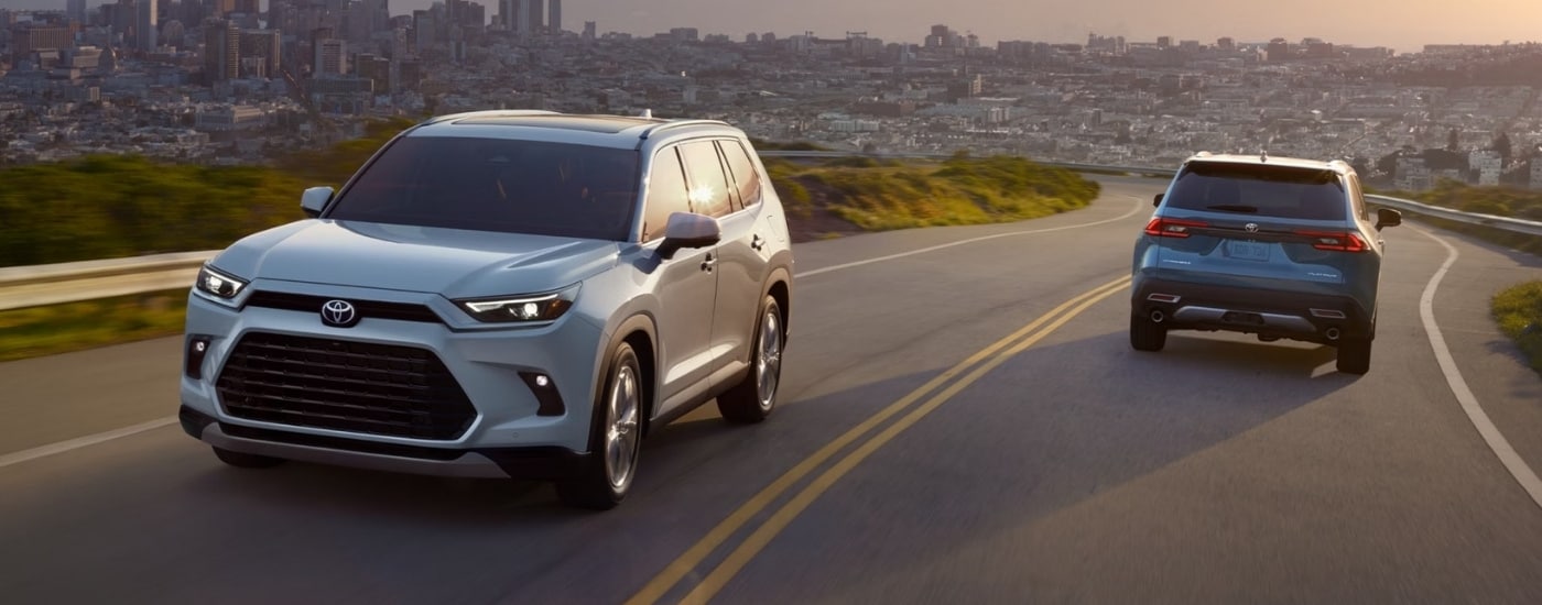 A grey and a blue 2025 Toyota Grand Highlander passing each other on the road.