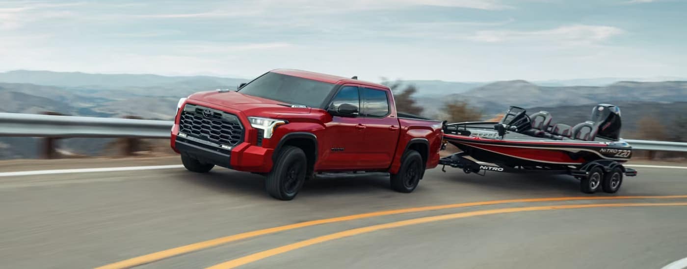 A red 2024 Toyota Tundra Limited Crewmax is towing a boat on a winding road.