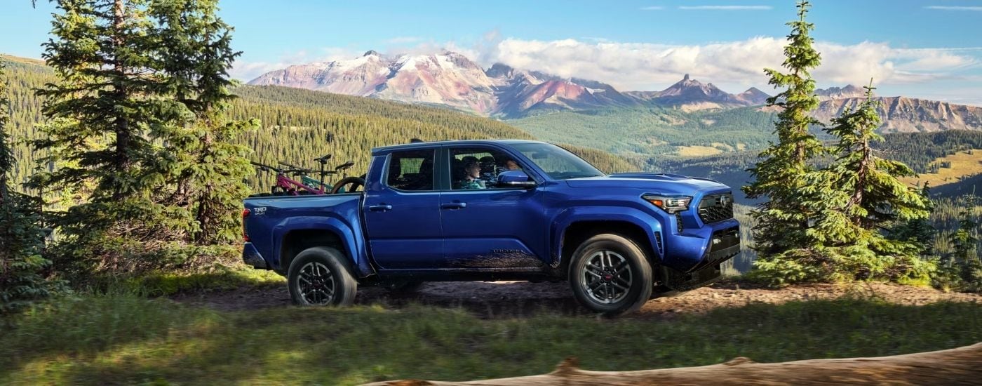 A blue 2024 Toyota Tacoma TRD Sport driving on a trail up a mountainside.
