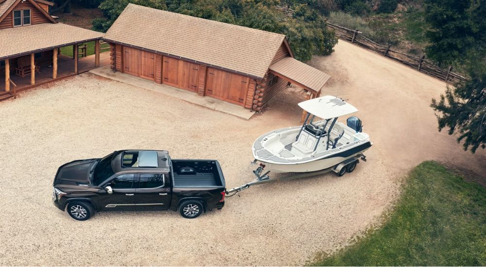 A brown 2024 Toyota Tundra is shown towing a boat near a cabin after leaving a Toyota dealer.