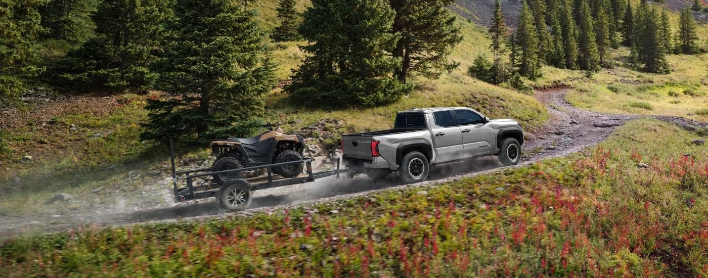 A grey 2025 Toyota Tacoma from the side while towing an ATV.