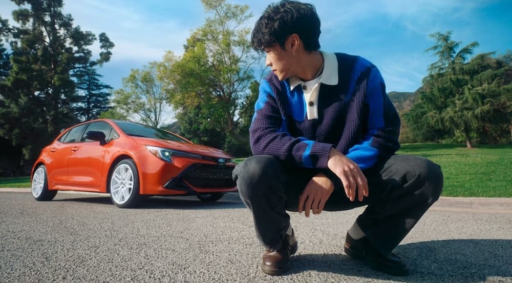 A person standing near an orange 2026 Toyota Corolla Hatchback.