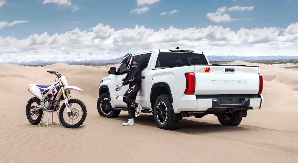 A white 2025 Toyota Tundra SR5 CrewMax is shown parked near a dirt bike.