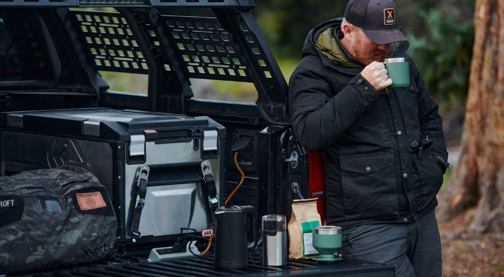 A man drinking coffee made using the in-bed power supply of his 2024 Toyota Tacoma Trailhunter.
