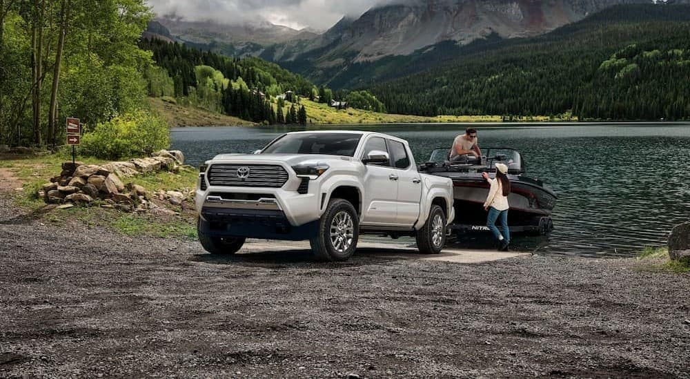 A white 2024 Toyota Tacoma Limited is shown towing a boat near a lake.