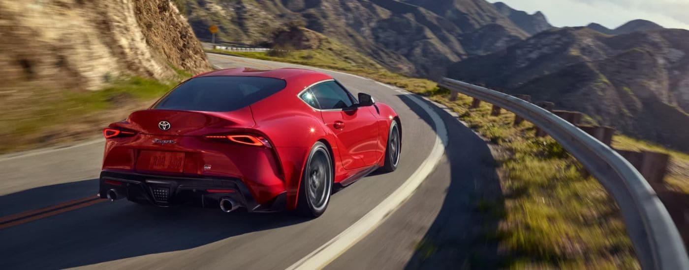 A red 2023 Toyota GR Supra is shown driving on a winding mountain road.