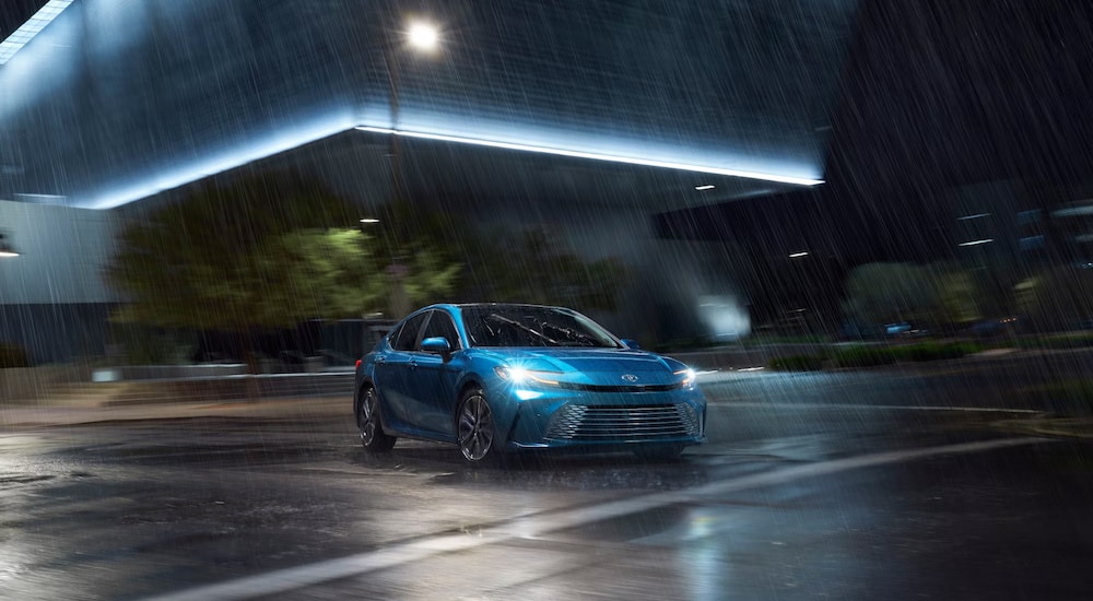 A blue 2025 Toyota Camry Hybrid XLE driving in the rain at night.