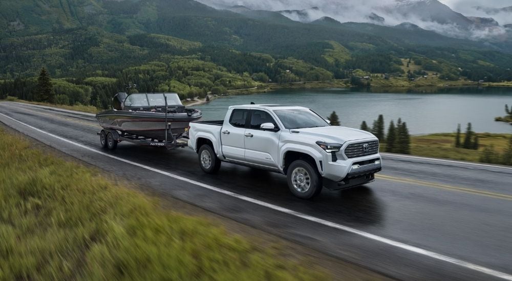 A white 2024 Toyota Tacoma Limited towing a boat past a lake.