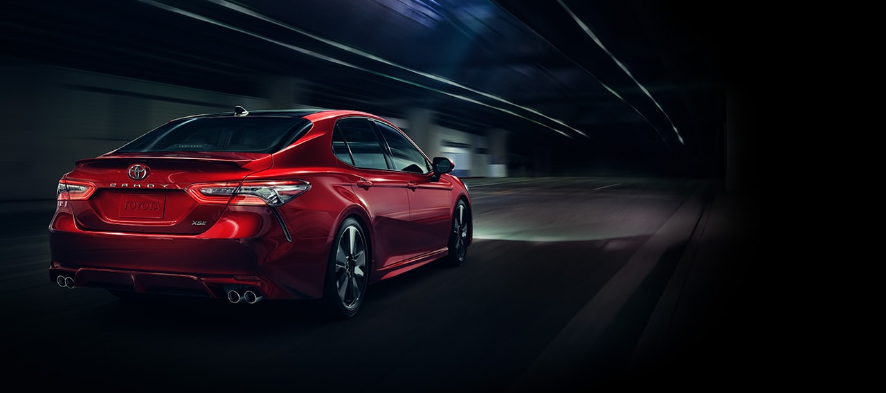 Rear three-quarters view of red 2018 Toyota Camry driving down dark road