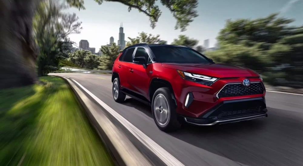 A red 2023 Toyota RAV4 Prime for sale is shown driving near a city.