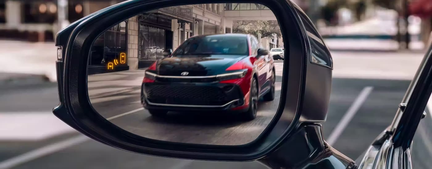A red 2023 Toyota Crown is shown in a side mirror driving on a city street.