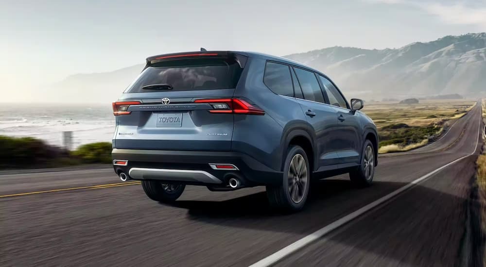 A blue 2024 Toyota Grand Highlander Platinum is shown from the rear driving on an open road.