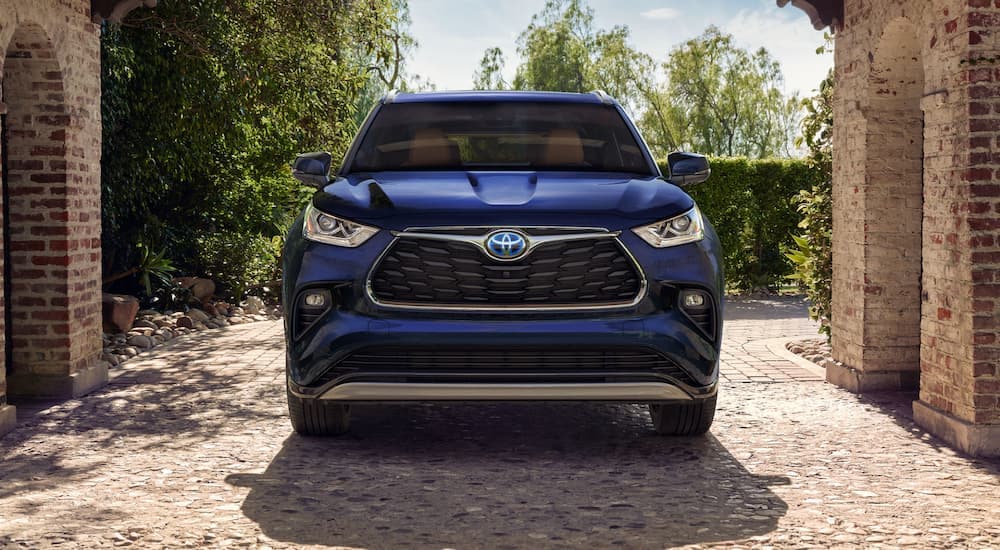 A blue 2023 Toyota Highlander Hybrid Platinum is shown from the front parked under a brick arch.