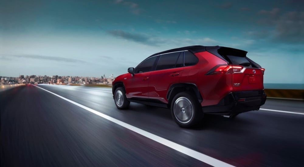 A red 2023 Toyota RAV4 is shown from the rear driving near a city.