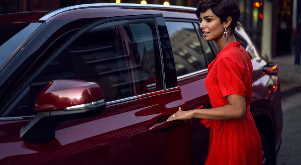 A woman is shown opening the door of a 2023 Toyota Highlander Hybrid Platinum in a city.