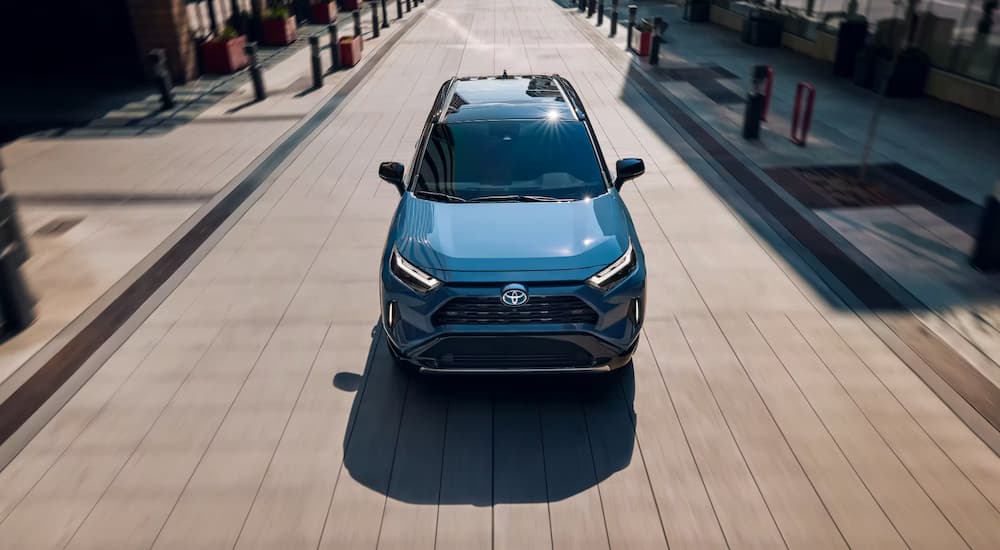 A blue 2023 Toyota RAV4 Hybrid is shown from the front driving on a city street.