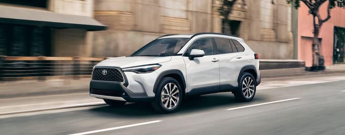 A white 2024 Toyota Corolla Cross is shown driving on a city street.