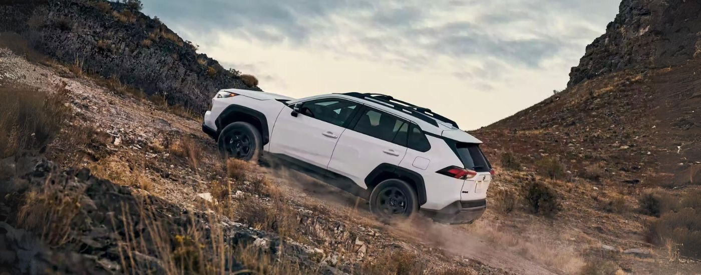 Side angle view of a white 2024 Toyota RAV4 TRD driving off-road up a hill.