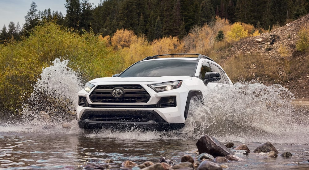 A white 2024 Toyota RAV4 TRD splashing through water while off-roading.
