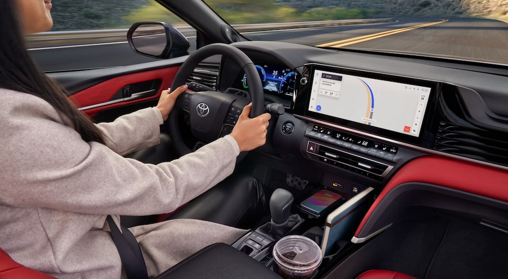 A woman driving in the red and black interior of a 2025 Toyota Camry Hybrid XSE for sale.