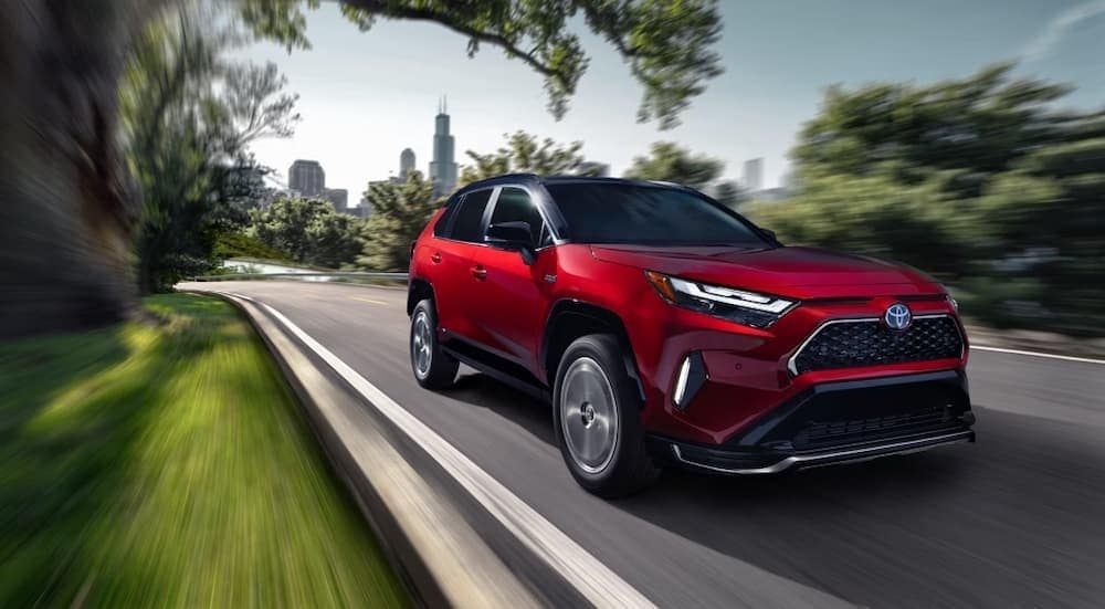 A red 2024 Toyota RAV4 Prime for sale in New York City is shown driving near a city.