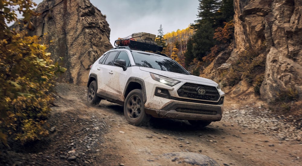 A white 2024 Toyota RAV4 TRD driving off-road with cargo on the roof.