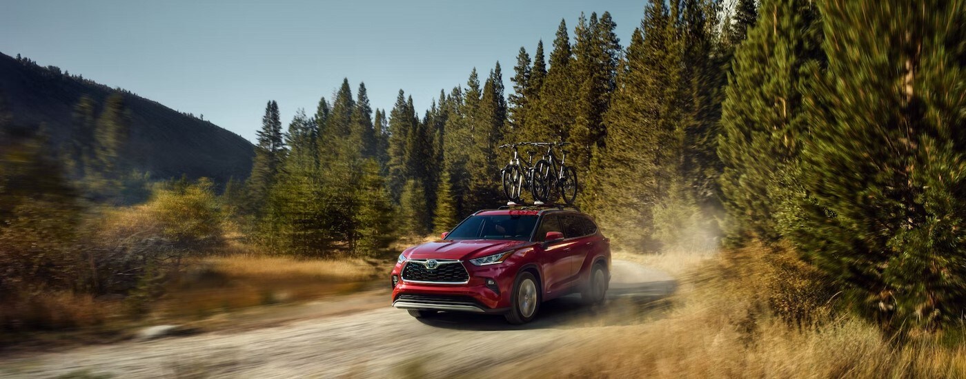 A red 2024 Toyota Highlander Platinum Hybrid is shown driving on a dirt path.
