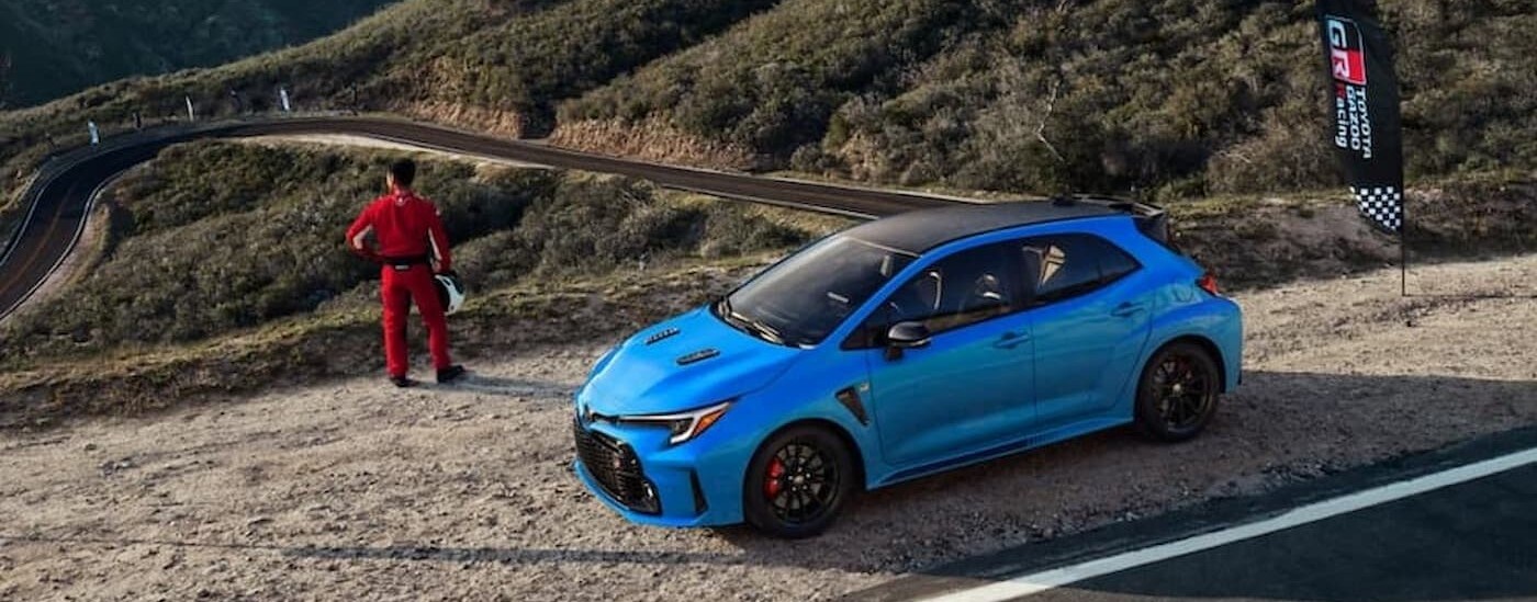 A blue 2024 Toyota GR Corolla is shown parked near a racecar driver.