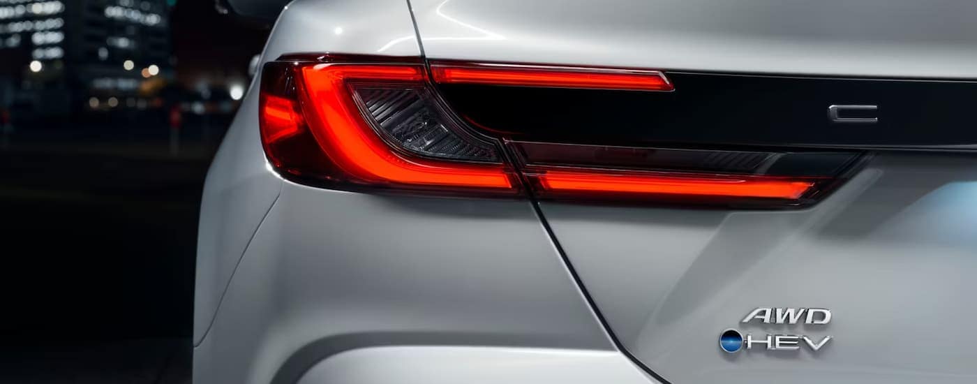 A close up of the rear brakelight on a white 2025 Toyota Camry Hybrid for sale at night.