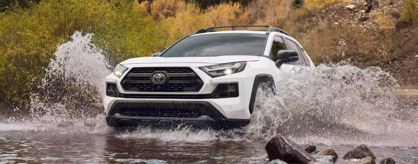 A white 2024 Toyota RAV4 TRD fording a shallow river.