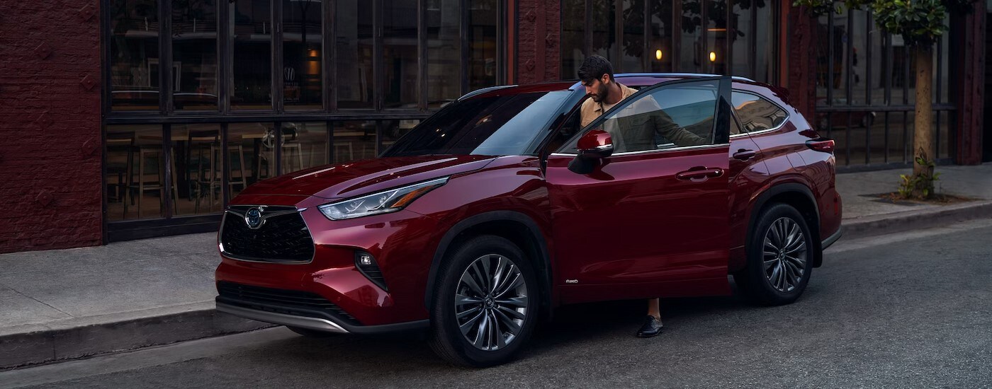 A red 2024 Toyota Highlander Platinum Hybrid for sale in New York City is shown parked on a city street.
