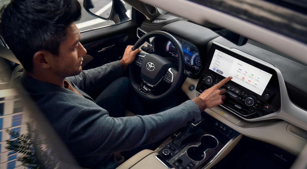 A person is shown touching the infotainment screen in a 2024 Toyota Highlander Hybrid Platinum.