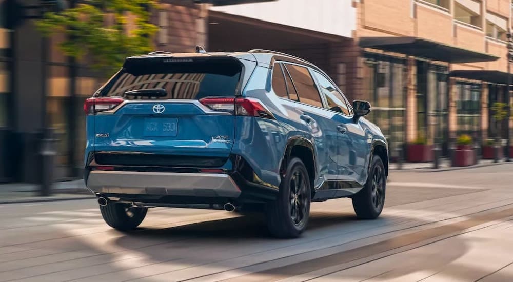 Rear view of a blue 2022 Toyota RAV4 Hybrid XSE driving on a city street.
