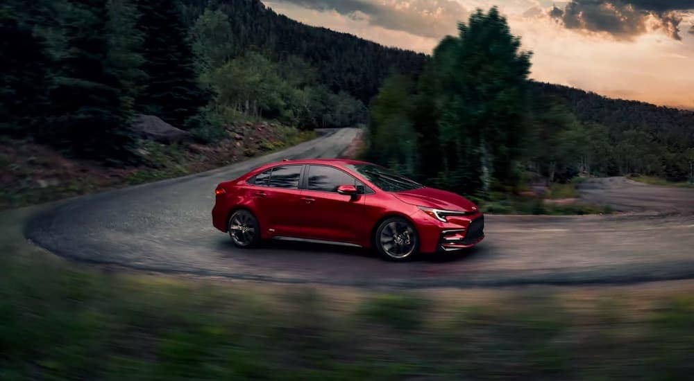 A red 2023 Toyota Corolla Hybrid is shown from the side on a winding road after leaving a used Toyota dealership.