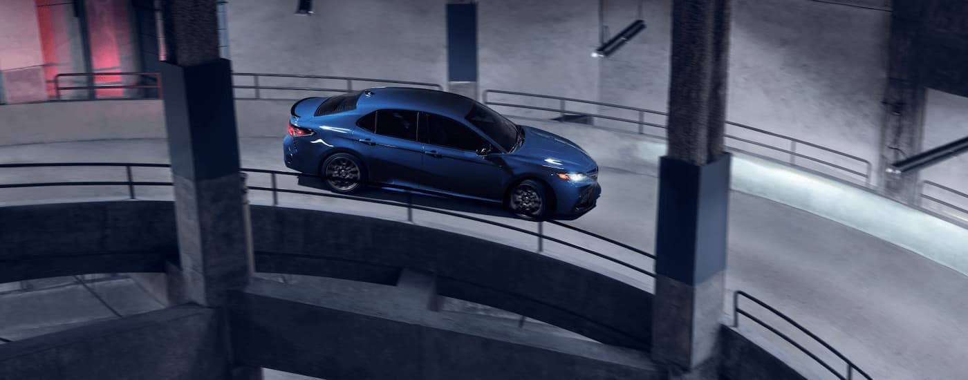 A blue 2024 Toyota Camry SE Hybrid Nightshade driving down a parking garage ramp.