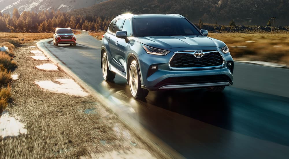 A blue and a red 2023 Toyota Highlander are shown from the front while driving down the road.