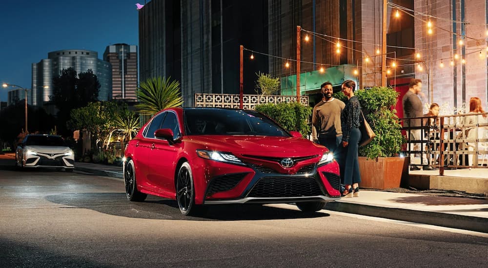 A red 2023 Toyota Camry is shown parked on the side of a city street.