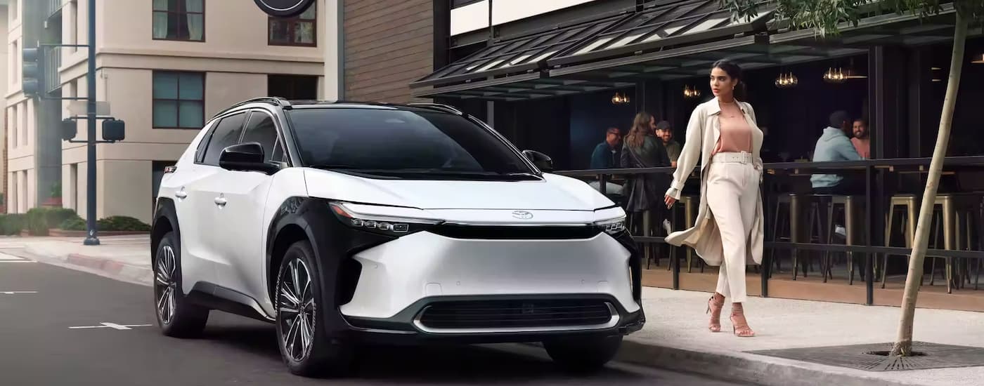 A woman is shown walking past a white 2022 Toyota bZ4X parked outside of a cafe.