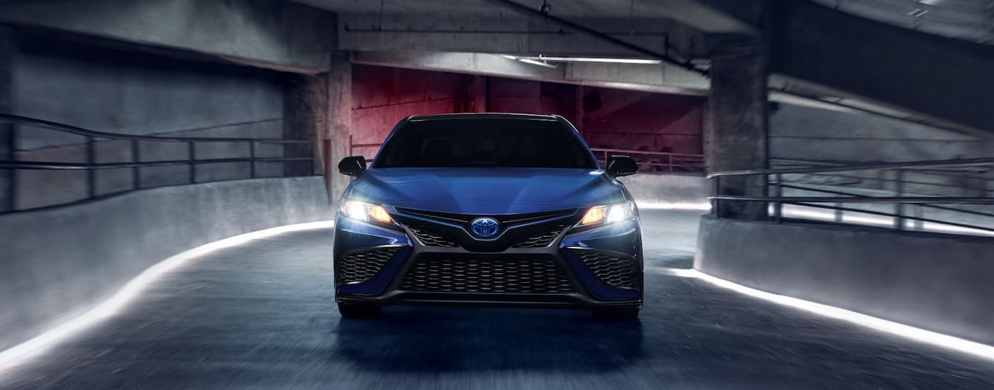 A grey 2024 Toyota Camry SE Hybrid Nightshade is shown from the front driving down a parking garage ramp.