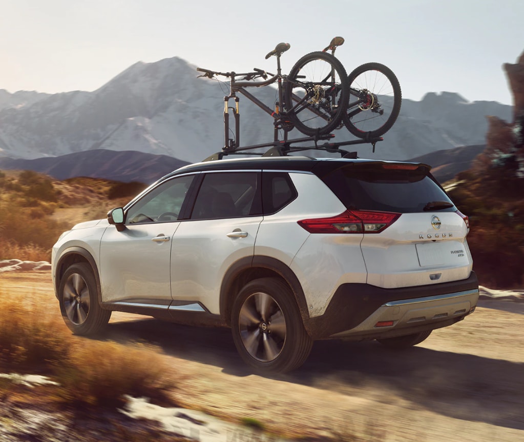 White 2021 Nissan Rogue Driving Off Road With Bicycle on Bike Rack on Roof