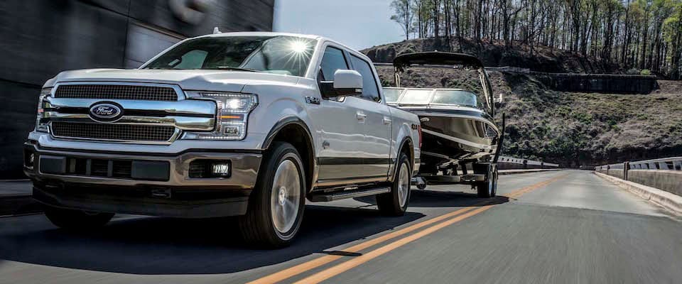 2019 Ford F-150 A white 2019 Ford F-150 towing a boat down a road