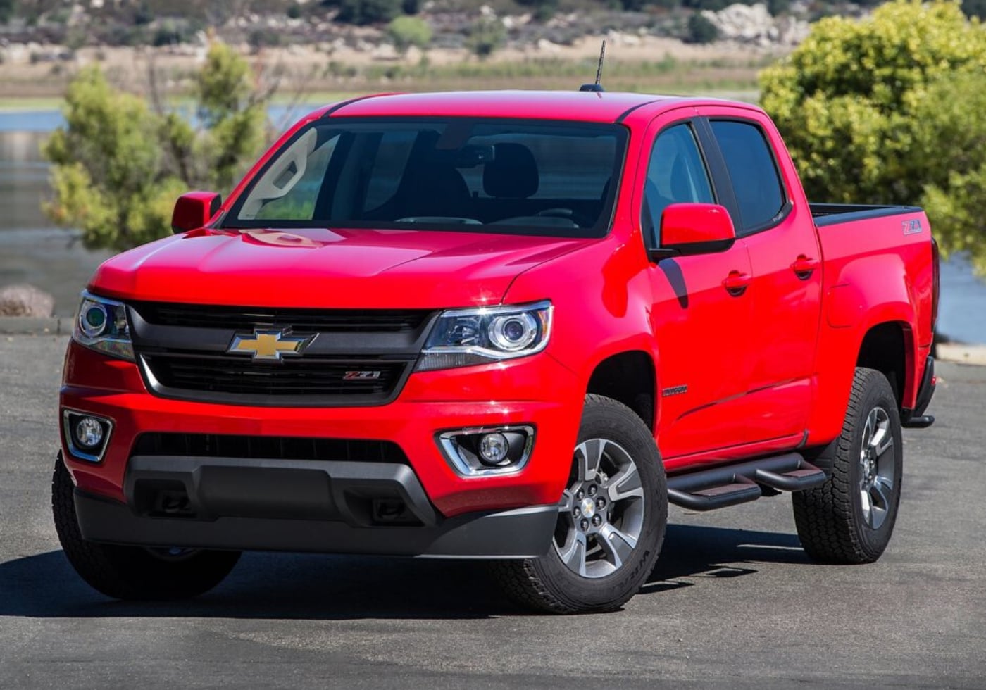 Red 2016 Chevrolet Colorado parked on an asphalt parking lot overlooking a lake