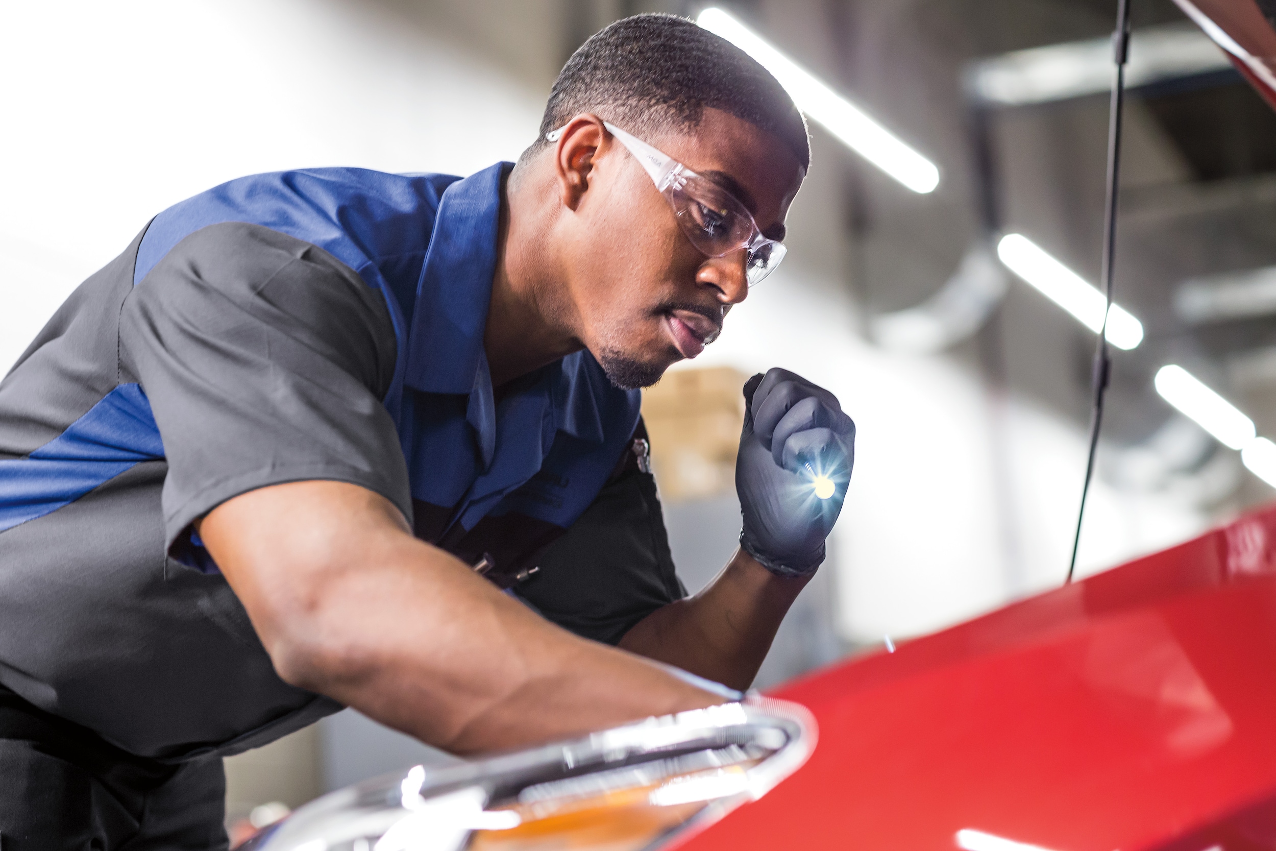 Man with safety goggles inspecting inside a red Subaru with a small flashlight