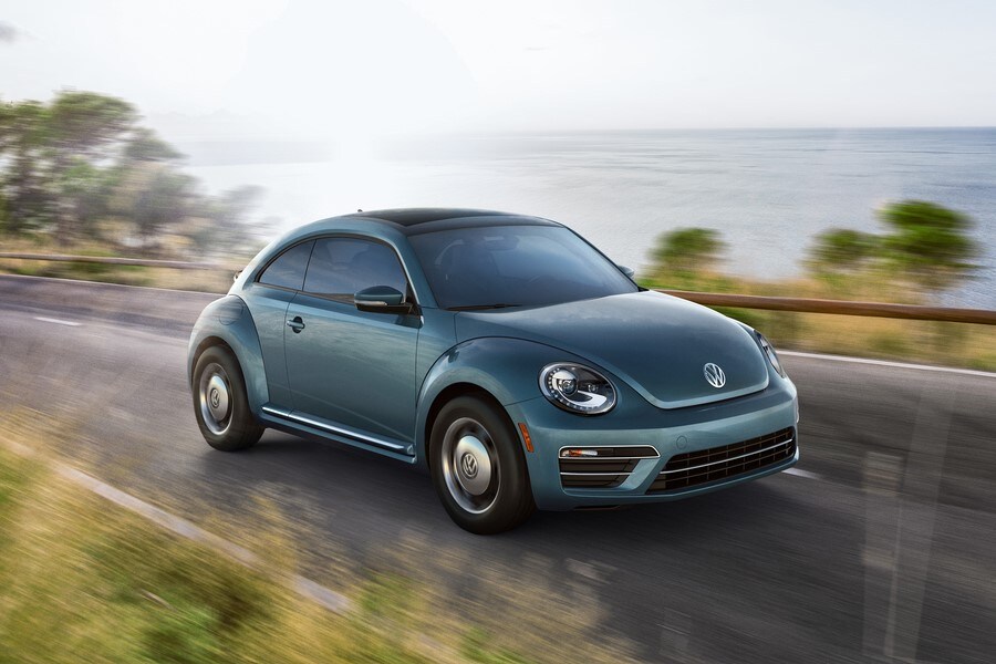 teal Volkswagen Beetle driving along the coast